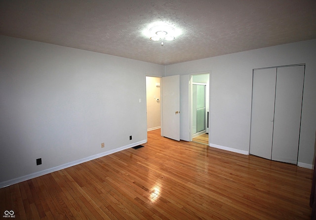 unfurnished bedroom with visible vents, connected bathroom, a textured ceiling, light wood-type flooring, and baseboards