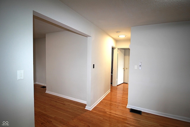 corridor with light wood-type flooring, visible vents, and baseboards