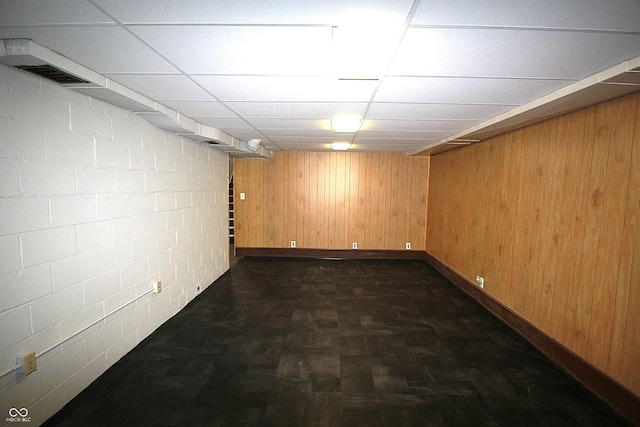 finished below grade area featuring visible vents, a drop ceiling, concrete block wall, and wooden walls