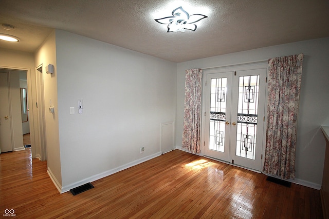 interior space featuring a textured ceiling, visible vents, baseboards, french doors, and hardwood / wood-style floors