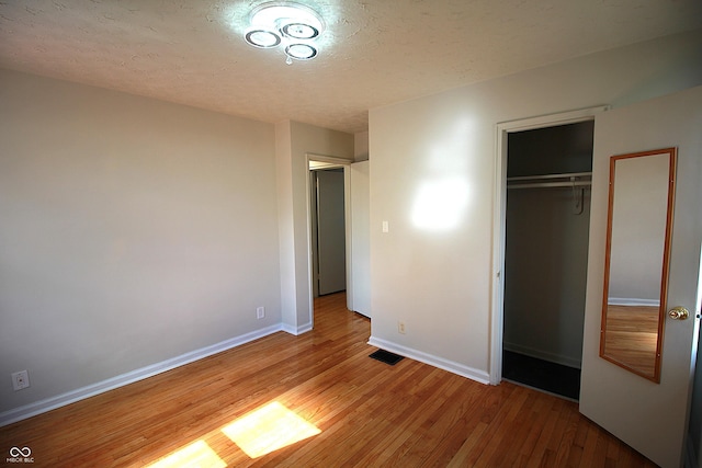 unfurnished bedroom with a textured ceiling, a closet, baseboards, and wood finished floors