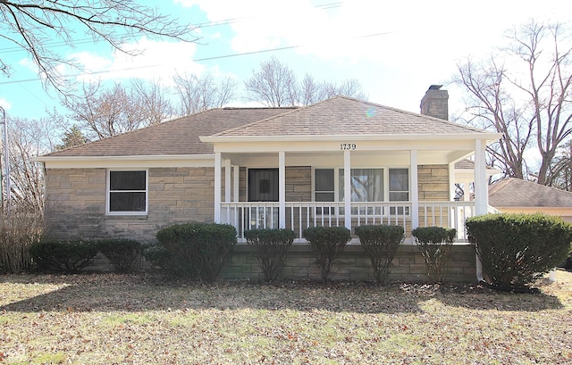 view of front of property with a shingled roof, covered porch, a chimney, and stone siding