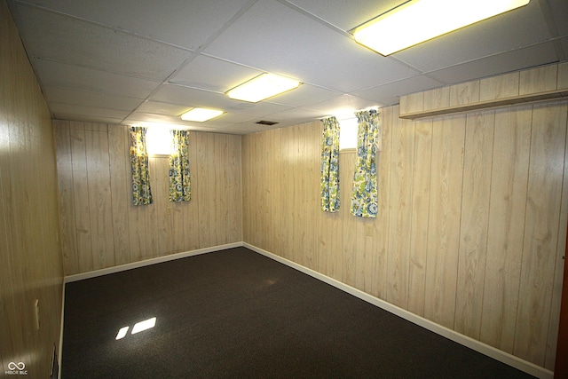 finished below grade area featuring wood walls, visible vents, baseboards, and a drop ceiling