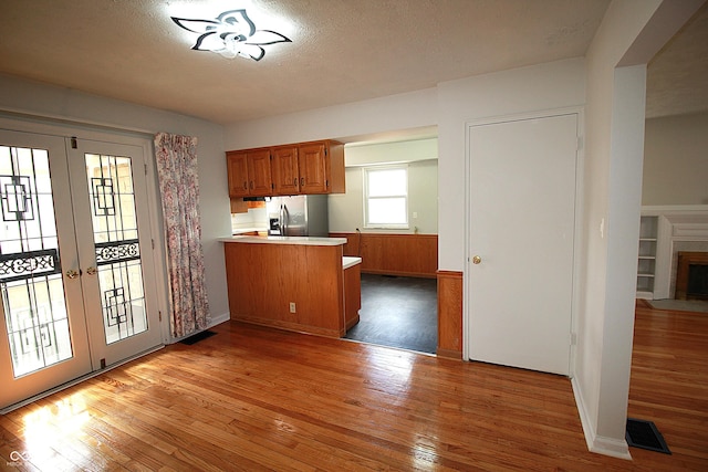 kitchen featuring light wood-style flooring, a fireplace with flush hearth, french doors, brown cabinetry, and stainless steel fridge