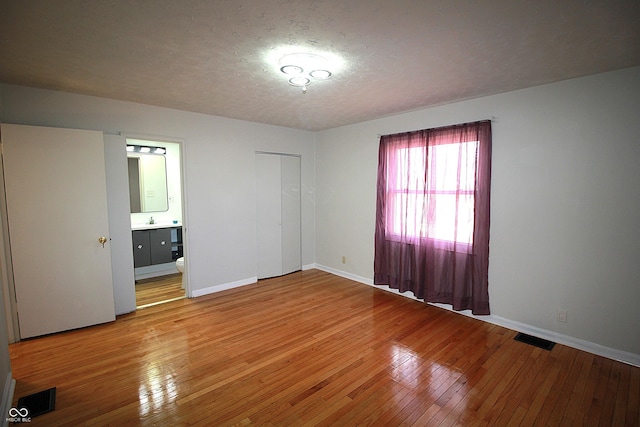 unfurnished bedroom with a textured ceiling, light wood-type flooring, and visible vents