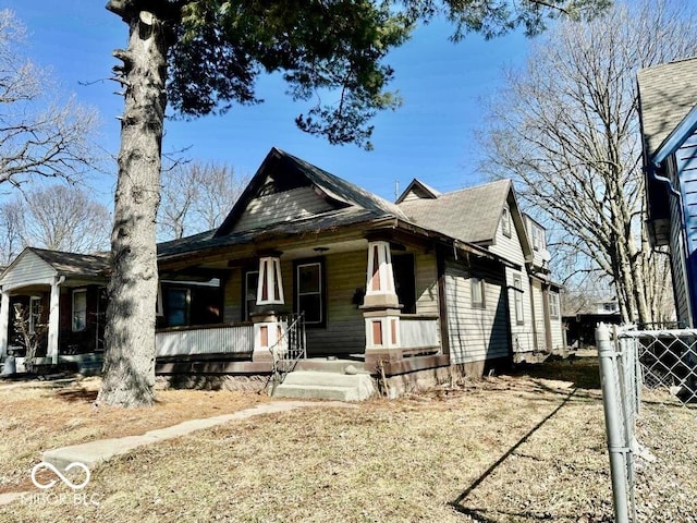 view of front facade featuring a shingled roof, fence, and a porch