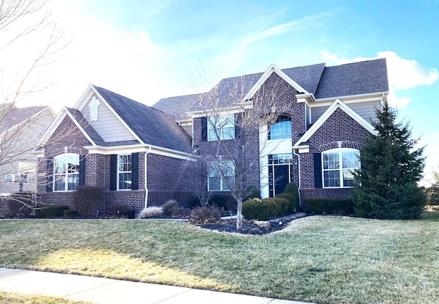 view of front of house with brick siding, a front lawn, and roof with shingles