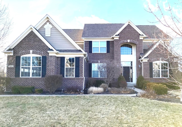 view of front of house with brick siding, a front lawn, and roof with shingles