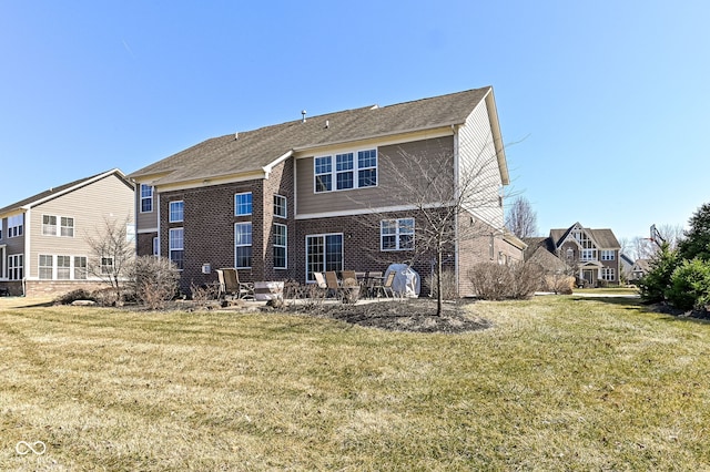 rear view of property featuring a patio, a yard, and brick siding