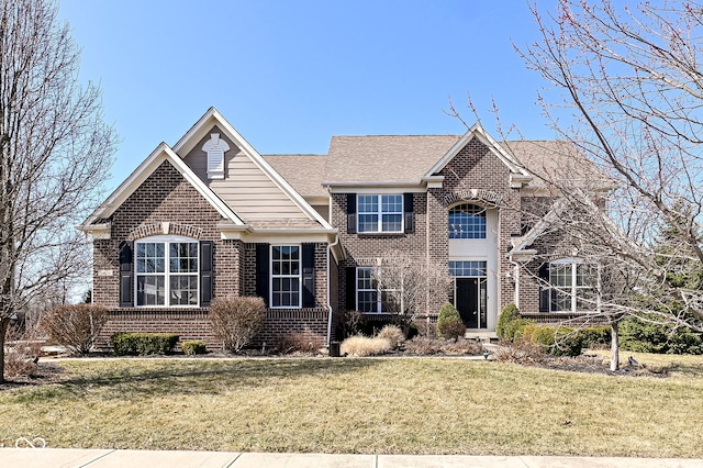 traditional-style house featuring a front lawn, brick siding, and roof with shingles