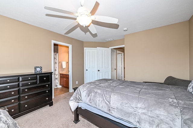 bedroom featuring visible vents, light colored carpet, connected bathroom, and a ceiling fan