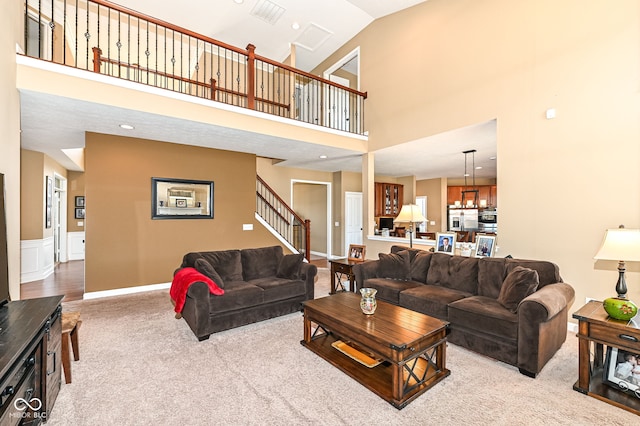 carpeted living area with a wainscoted wall, high vaulted ceiling, a notable chandelier, recessed lighting, and stairway