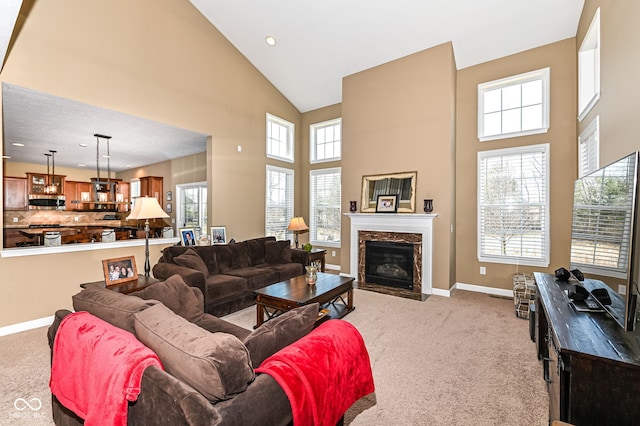 living area featuring baseboards, light carpet, high vaulted ceiling, and a high end fireplace