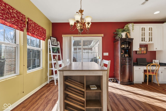 dining area featuring a notable chandelier, wood finished floors, visible vents, baseboards, and built in desk