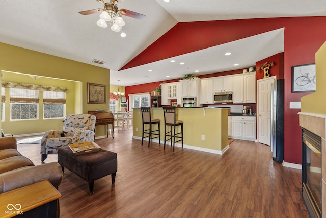 living area with baseboards, visible vents, a tiled fireplace, dark wood-type flooring, and ceiling fan with notable chandelier