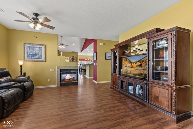 living area featuring a tile fireplace, dark wood-style flooring, a textured ceiling, and baseboards