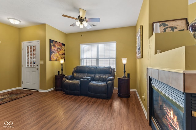 living area featuring a ceiling fan, baseboards, a tiled fireplace, and wood finished floors