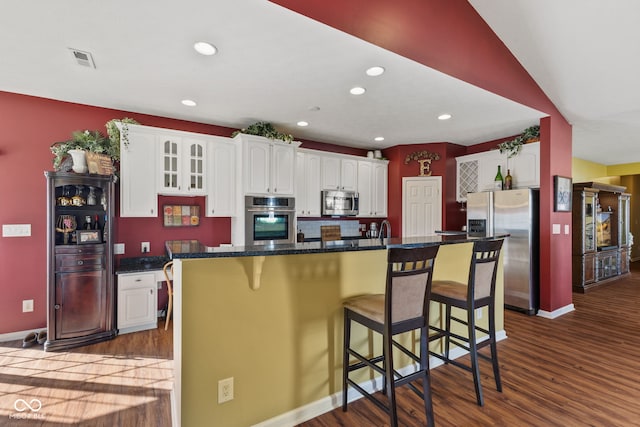 kitchen featuring visible vents, appliances with stainless steel finishes, a breakfast bar, dark wood-type flooring, and white cabinetry