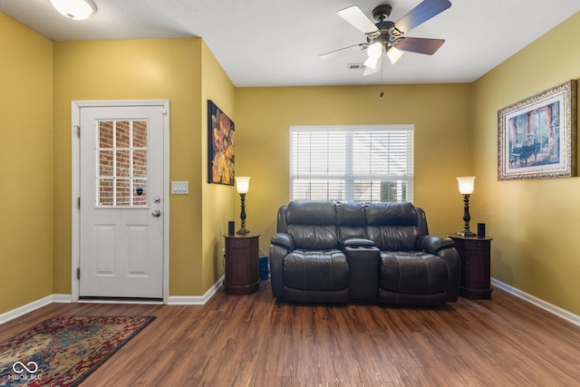 living room featuring a ceiling fan, visible vents, baseboards, and wood finished floors