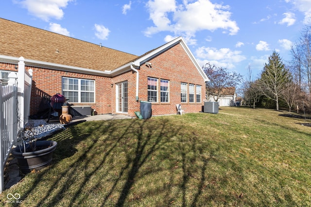 back of house featuring brick siding, a lawn, central AC, and fence