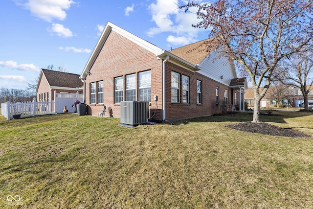 view of property exterior with a yard, central AC, brick siding, and fence