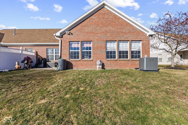 rear view of house with cooling unit, brick siding, a yard, and fence