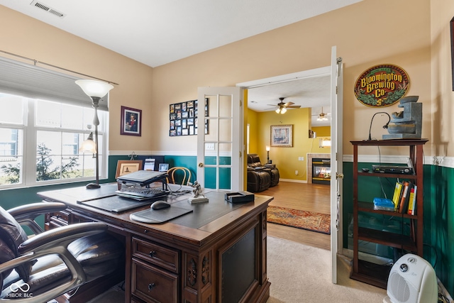 home office with light wood finished floors, visible vents, a ceiling fan, and a tile fireplace