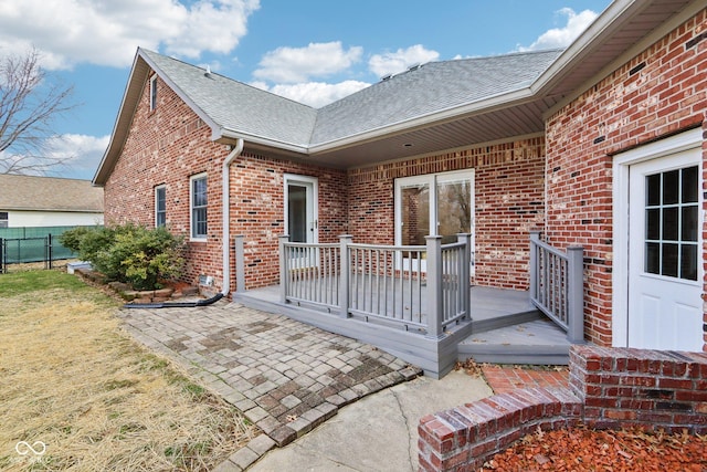 exterior space featuring brick siding, a yard, fence, and roof with shingles