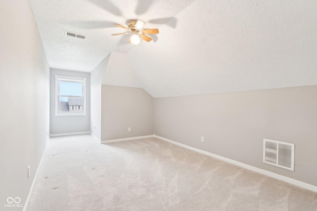 additional living space with light colored carpet, visible vents, vaulted ceiling, and a textured ceiling