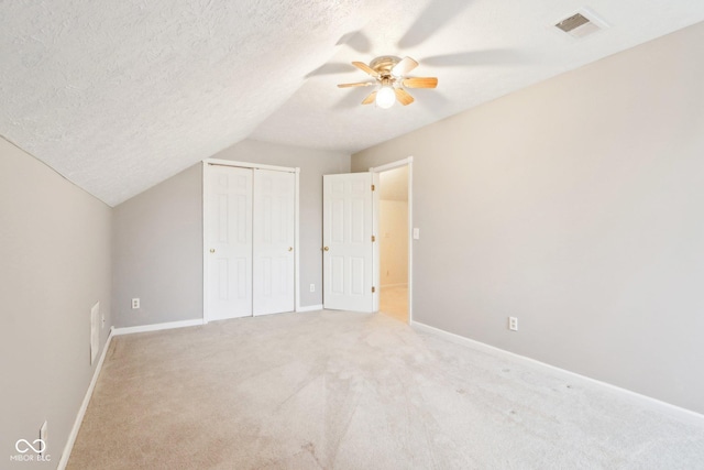 unfurnished bedroom featuring a textured ceiling, lofted ceiling, light colored carpet, visible vents, and a closet