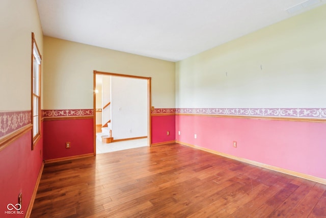 unfurnished room featuring wood-type flooring, visible vents, stairway, and baseboards