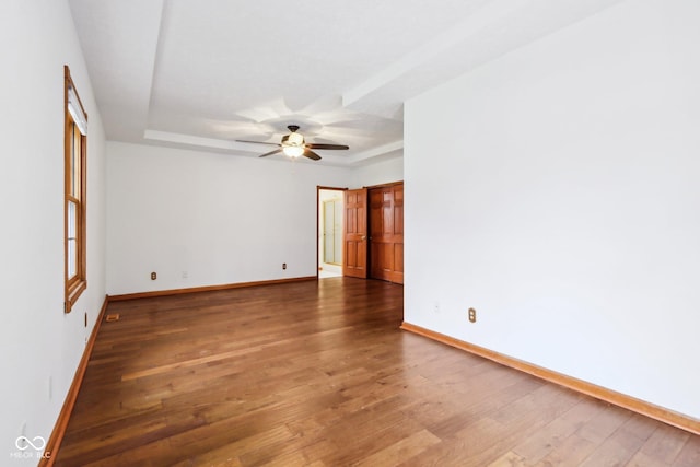 empty room featuring a tray ceiling, ceiling fan, baseboards, and hardwood / wood-style flooring