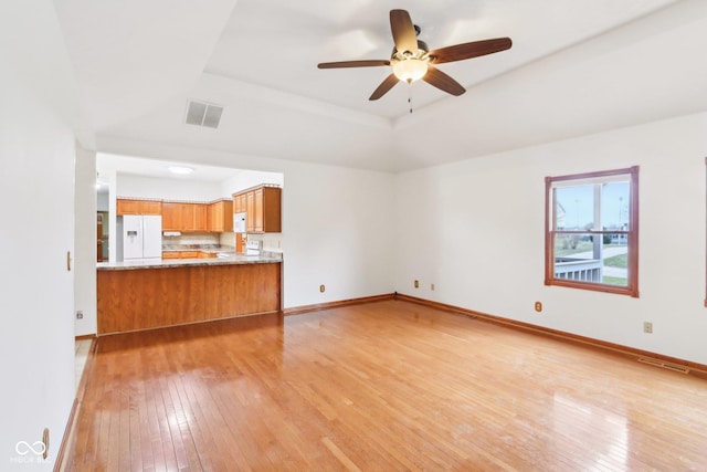 unfurnished living room with ceiling fan, light wood-style flooring, visible vents, baseboards, and a raised ceiling