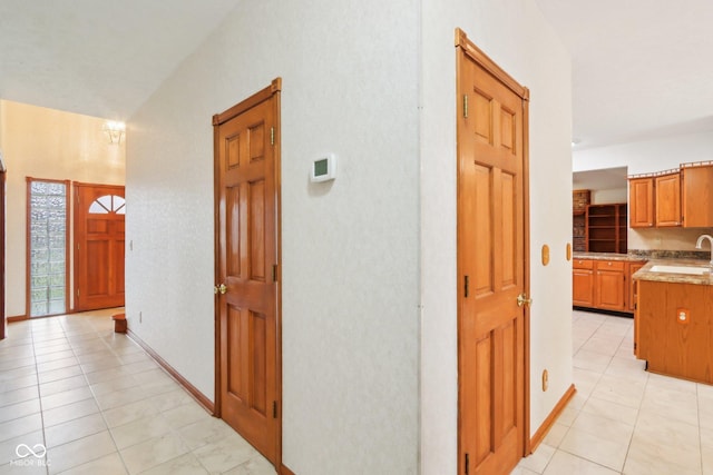 hall featuring light tile patterned floors, a sink, and baseboards