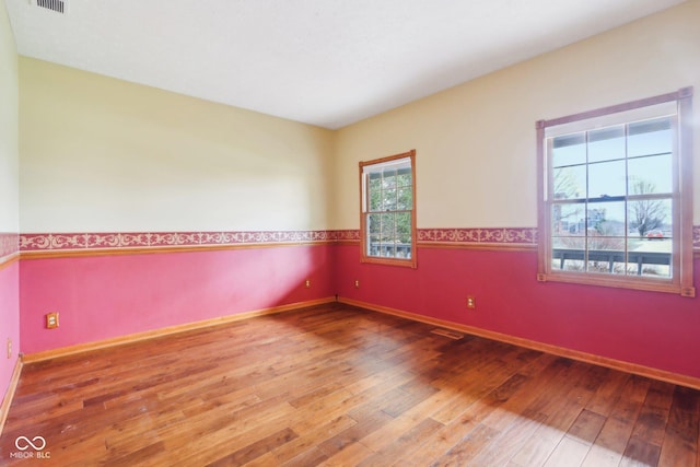 unfurnished room with visible vents, baseboards, and hardwood / wood-style flooring