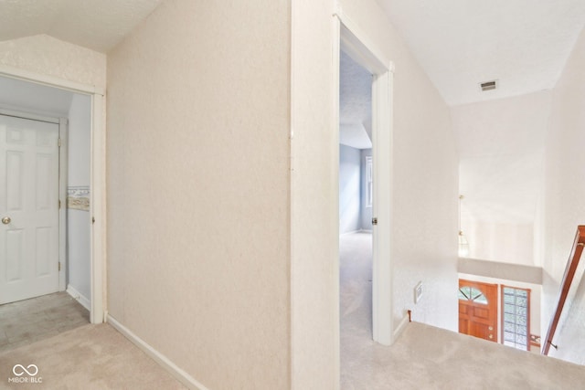 hall featuring visible vents, baseboards, lofted ceiling, carpet, and an upstairs landing