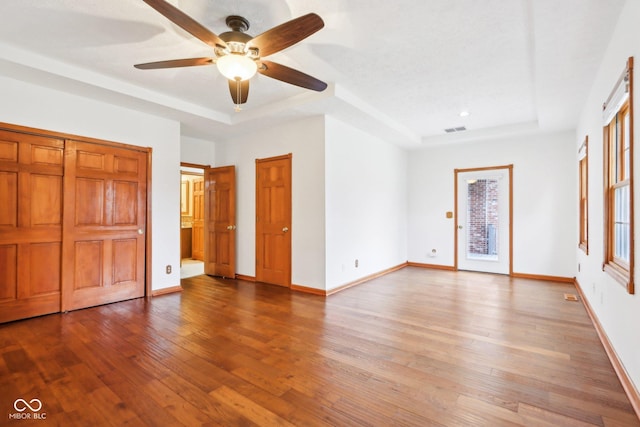 unfurnished bedroom with wood-type flooring, a tray ceiling, and baseboards