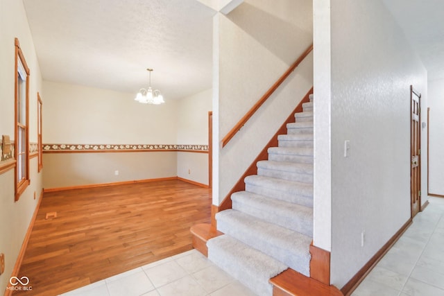 staircase with a notable chandelier, baseboards, and wood finished floors