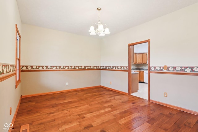 spare room featuring a chandelier, light wood-type flooring, visible vents, and baseboards