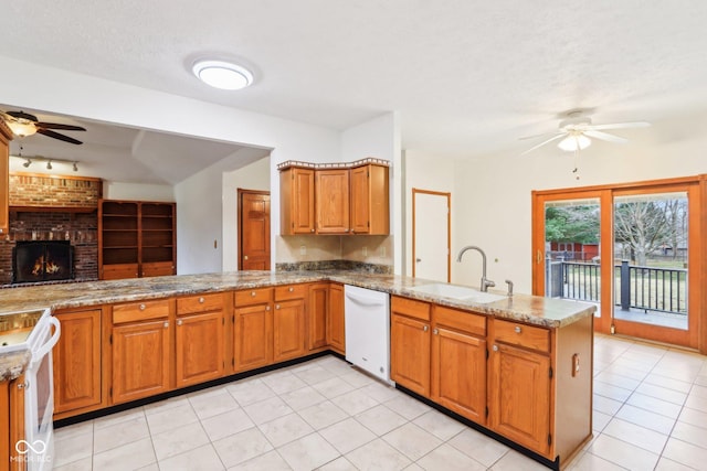 kitchen with ceiling fan, a peninsula, white appliances, a sink, and a brick fireplace