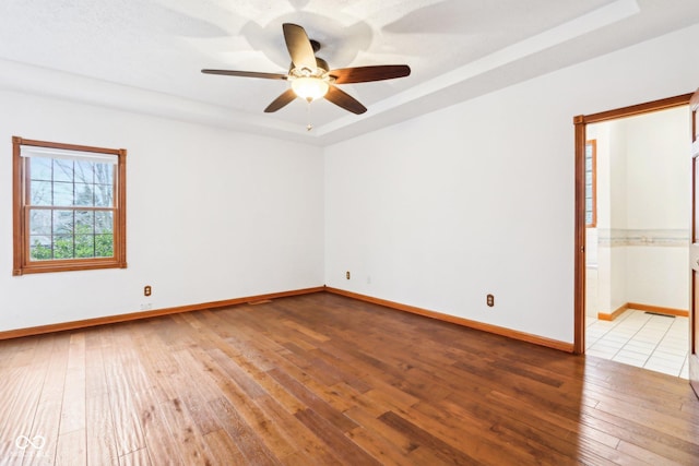 unfurnished room with a tray ceiling, baseboards, ceiling fan, and light wood finished floors