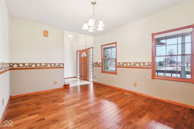 empty room featuring visible vents, a notable chandelier, baseboards, and hardwood / wood-style flooring