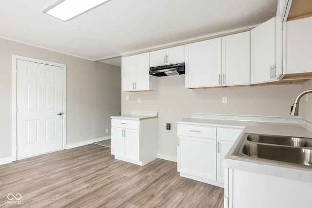 kitchen featuring under cabinet range hood, a sink, white cabinets, light countertops, and light wood finished floors