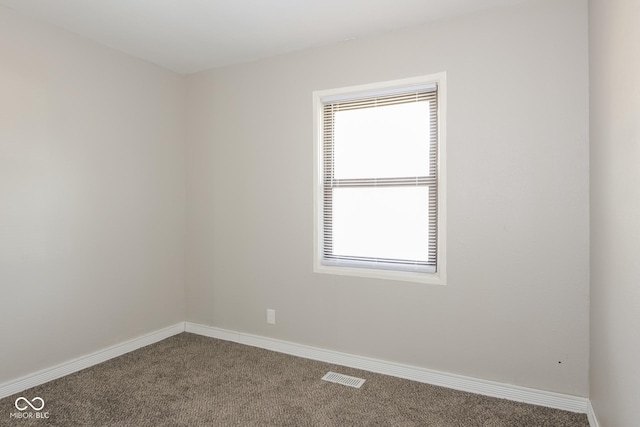 spare room with baseboards, visible vents, and dark carpet