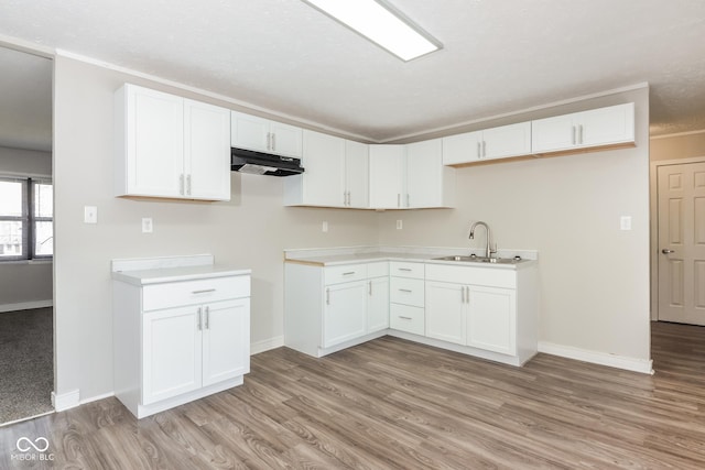 kitchen with baseboards, light wood-type flooring, under cabinet range hood, white cabinetry, and a sink