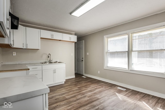 kitchen with visible vents, baseboards, white cabinets, wood finished floors, and a sink