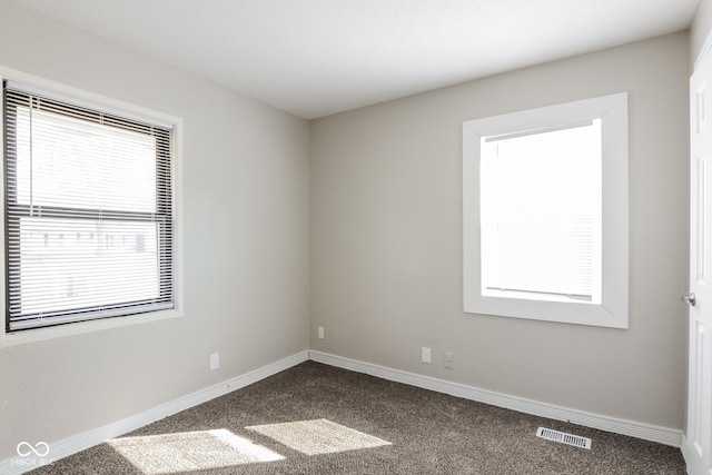 spare room with a wealth of natural light, dark carpet, and baseboards