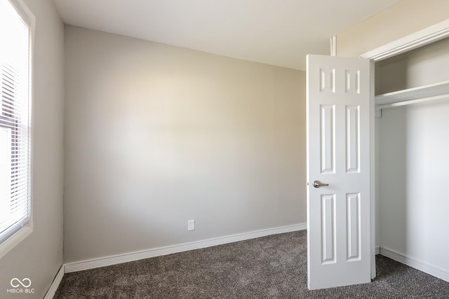 unfurnished bedroom with dark carpet and baseboards