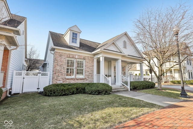 view of front of house with a front yard, a gate, fence, a porch, and brick siding