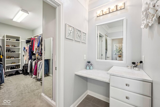 bathroom featuring a walk in closet, crown molding, baseboards, and tile patterned flooring